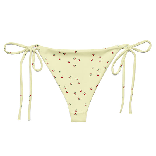 A yellow bikini bottom called the Cherry Orchard, made from recycled polyester with UPF 50+ sun protection. The bottoms feature a refreshing cream base with a vibrant cherry pattern and are available in sizes 2XS to 6XL. They are designed with soft, stret