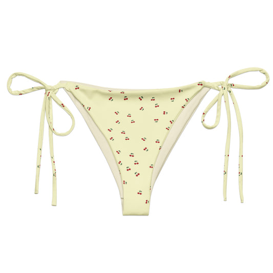 A yellow bikini bottom called the Cherry Orchard, made from recycled polyester with UPF 50+ sun protection. The bottoms feature a refreshing cream base with a vibrant cherry pattern and are available in sizes 2XS to 6XL. They are designed with soft, stret